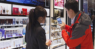 Traveler experiencing new online shopping methods ("click & go") with the help of a consultant at the Lancôme point of sale at Paris Charles de Gaulle Airport in France